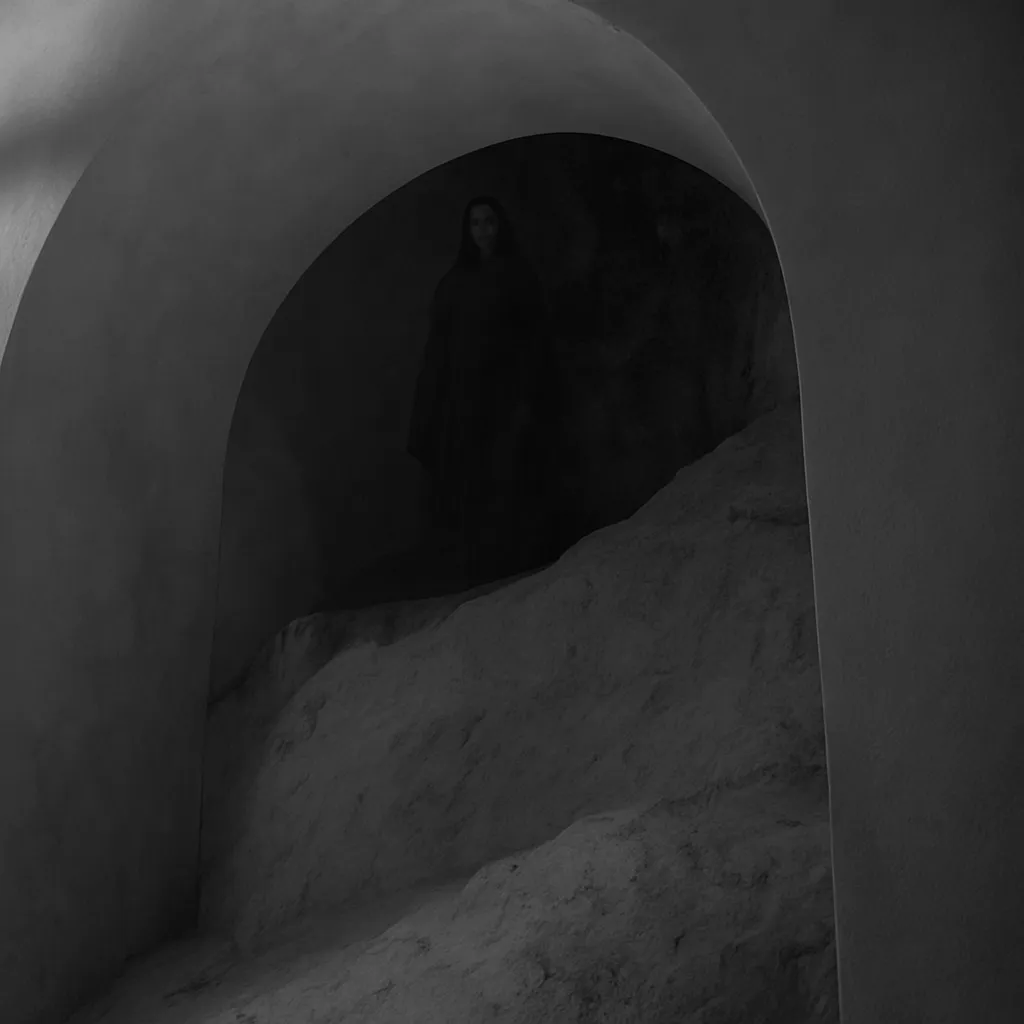 Apparizione spettrale di una monaca avvolta nell’ombra sotto un arco in pietra all’interno del Castello di Milazzo.